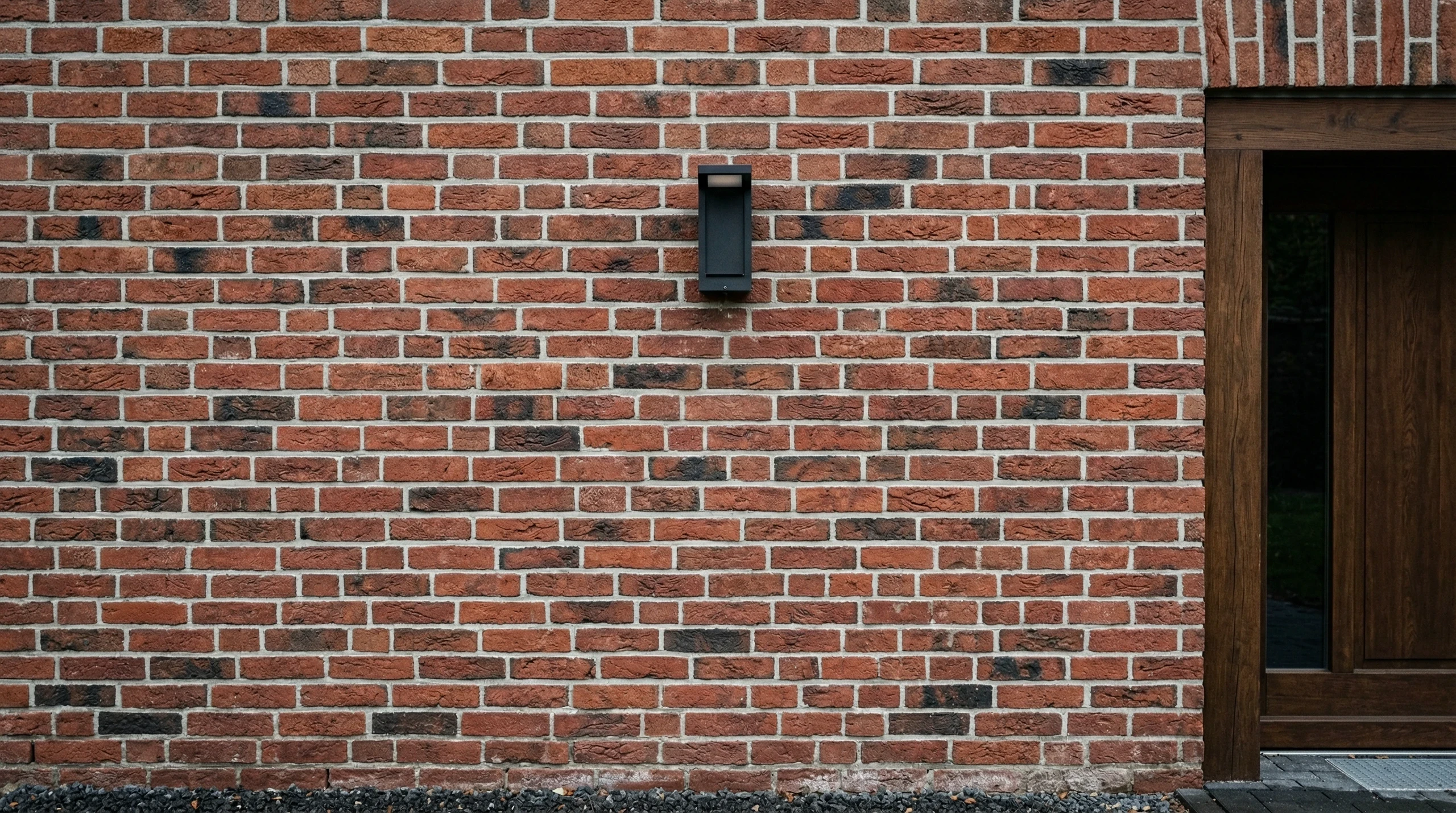 Rote Backsteinfassade mit moderner Außenleuchte und Holztürrahmen Fassade