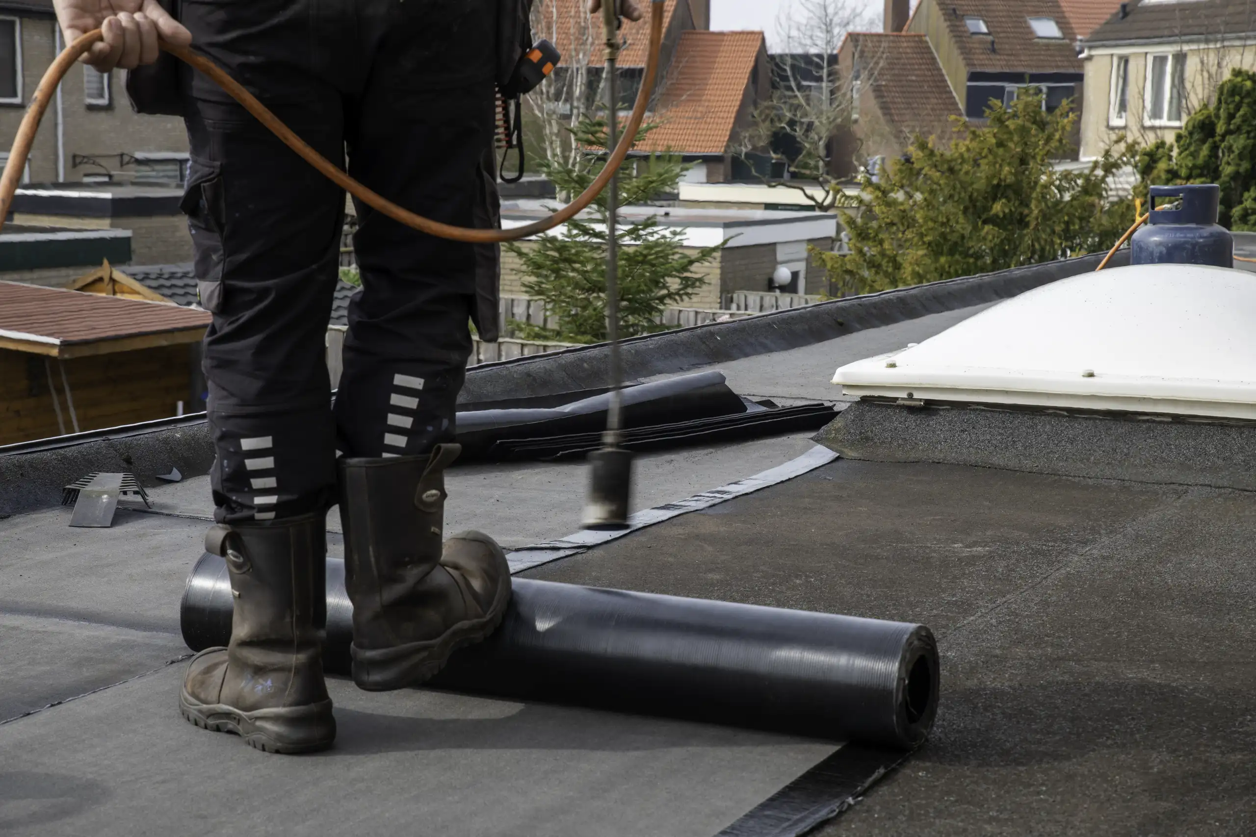Handwerker bei Abdichtungsarbeiten auf Flachdach mit Bitumenbahn und Heißluftföhn