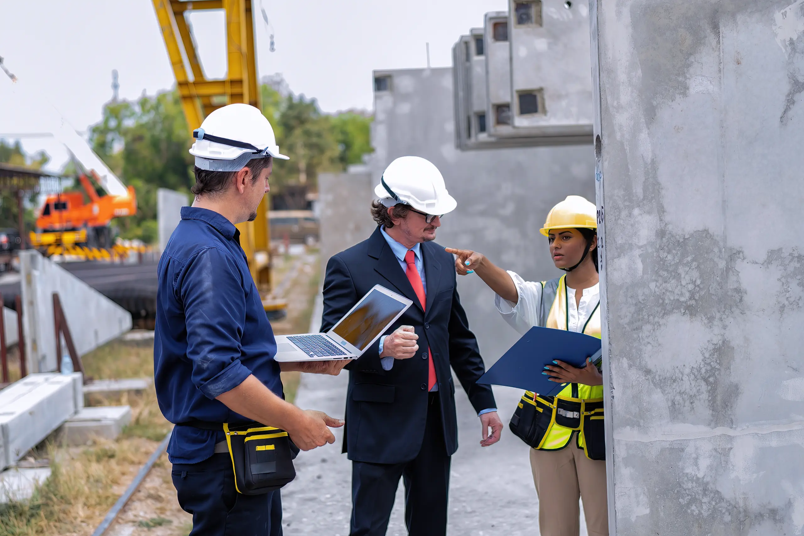 Bauleitung: Drei Fachleute in Schutzhelmen besprechen Baustelle mit Betonfertigteilen